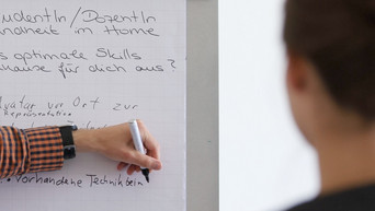 Eine Hand notiert mit einem Stift Stichpunkte auf einem Flipchart.