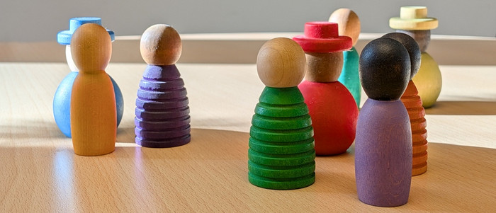 Kleine Holzfiguren stehen auf einem Tisch und sind angeordnet als würden sie diskutieren. Die Sonne beleuchtet die Szene von links.