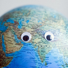 Earth globe with googly eyes on gray background
